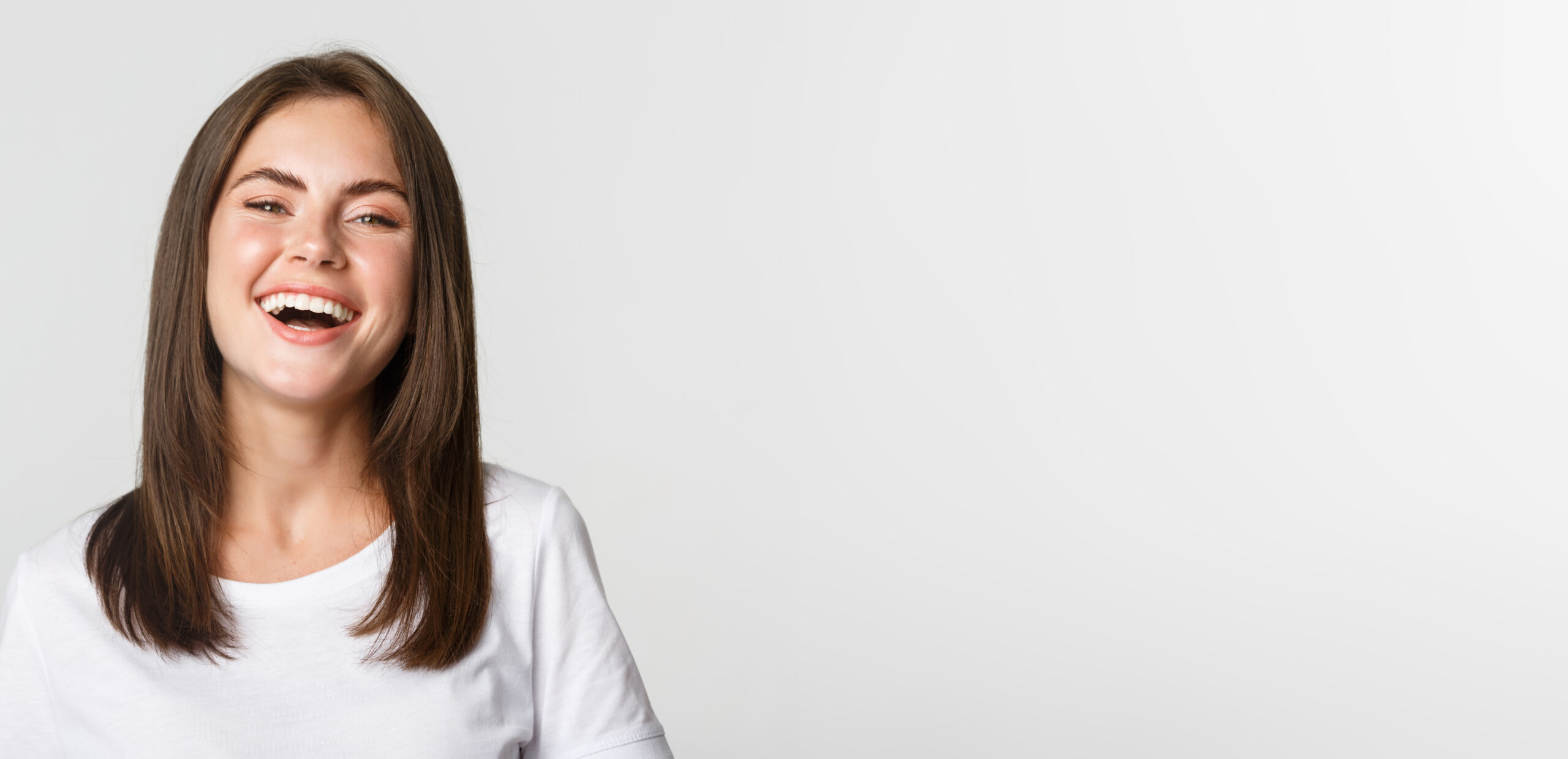 Close-up of happy brunette girl in white t-shirt laughing and smiling carefree at camera.
